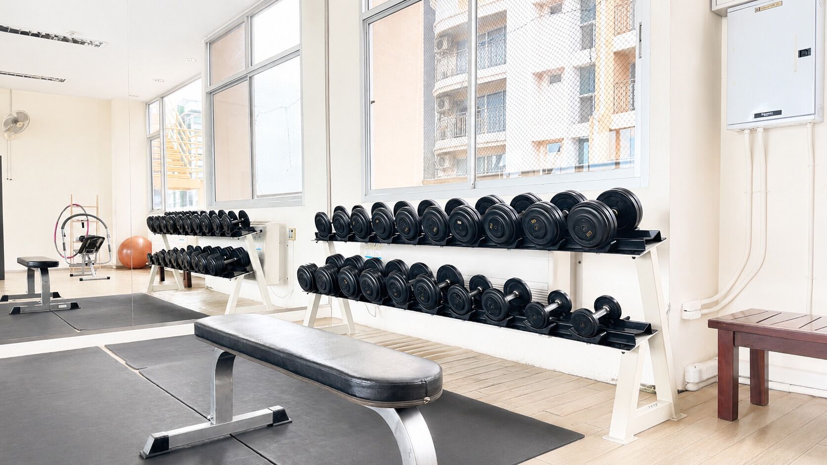 A gym with weightlifting equipment, a bench, and a large window.