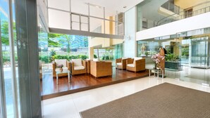A modern lobby with wicker furniture, glass walls, and indoor plants. - Olive Hotel & Residence Bangkok Sukhumvit 101 near True Digital Park (Bangkok)