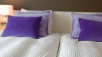 Een bed met witte beddengoed en twee paarse kussens.