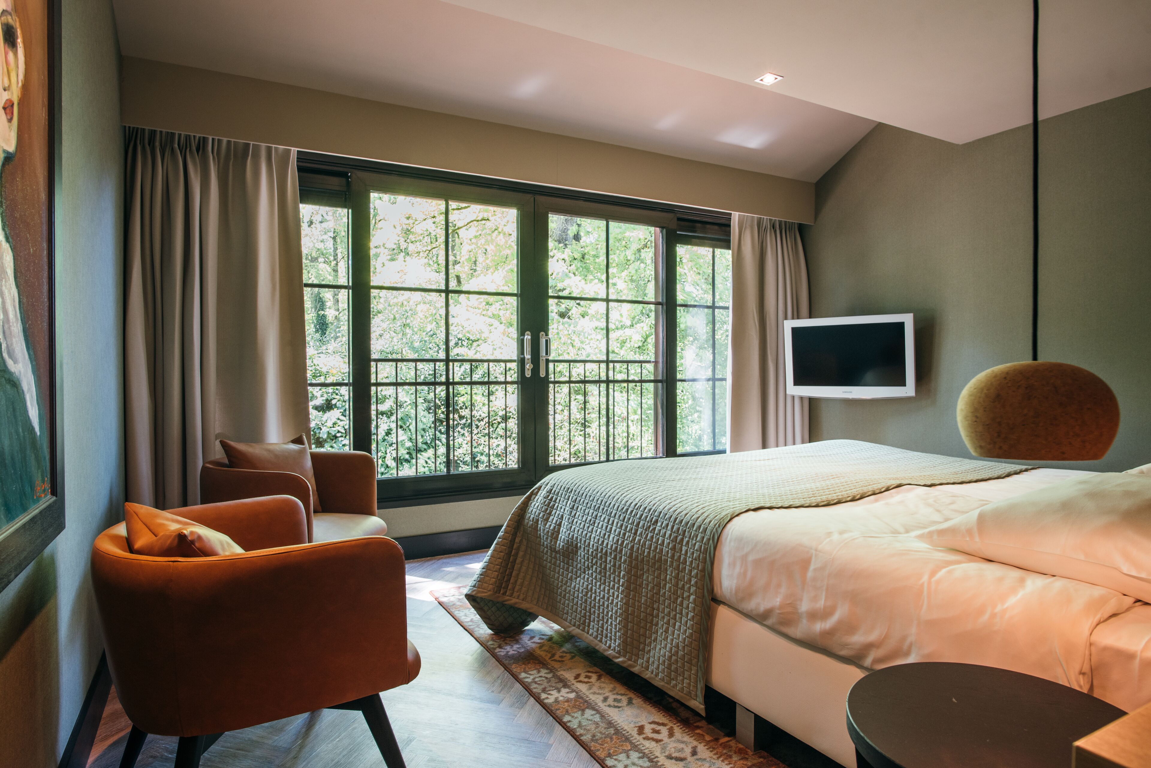 A bedroom with a large window, a bed, a chair, a TV, and a round table.
