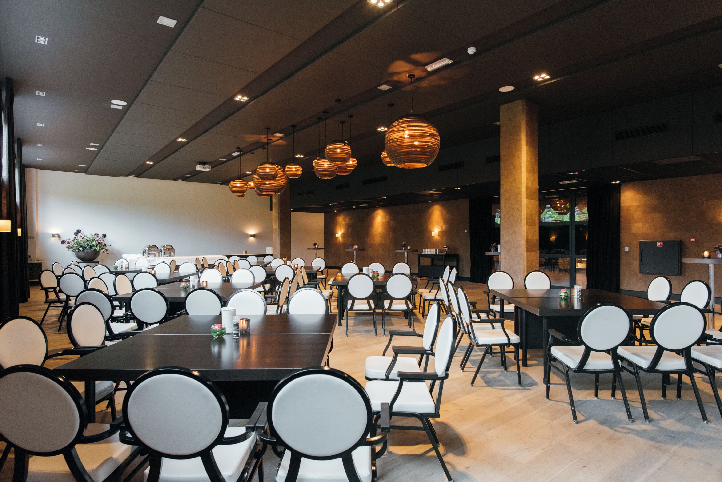 A spacious conference room with multiple tables and chairs, overhead lighting, and a neutral color scheme.