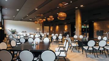 A spacious conference room with multiple tables and chairs, overhead lighting, and a neutral color scheme.