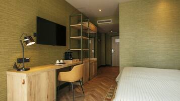 Una habitación de hotel con un escritorio de madera, una silla, una cama, un televisor montado en la pared y un armario.