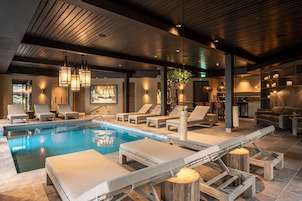 Un área de piscina interior moderna con sillones de descanso, techo de madera e iluminación ambiental.