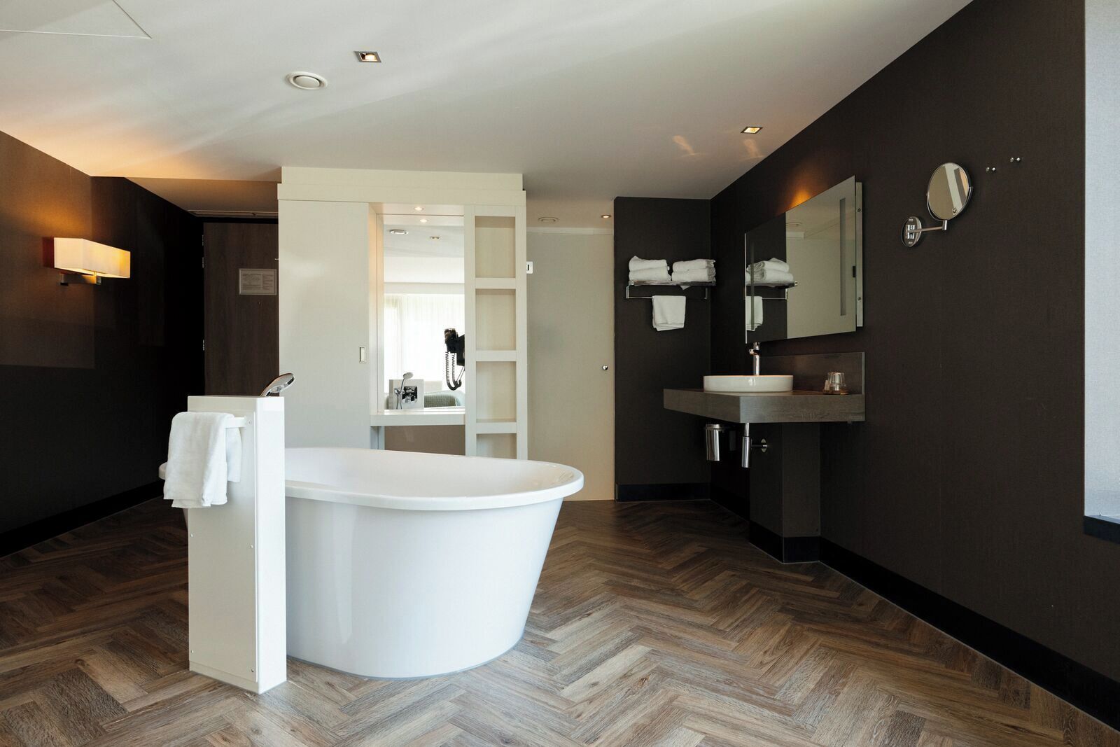 Un baño moderno con una bañera independiente, un tocador con espejo y un suelo de madera con diseño de espiga.