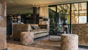 A spacious lobby with a large seating area, a coffee table, and a view of the outdoors through large windows.