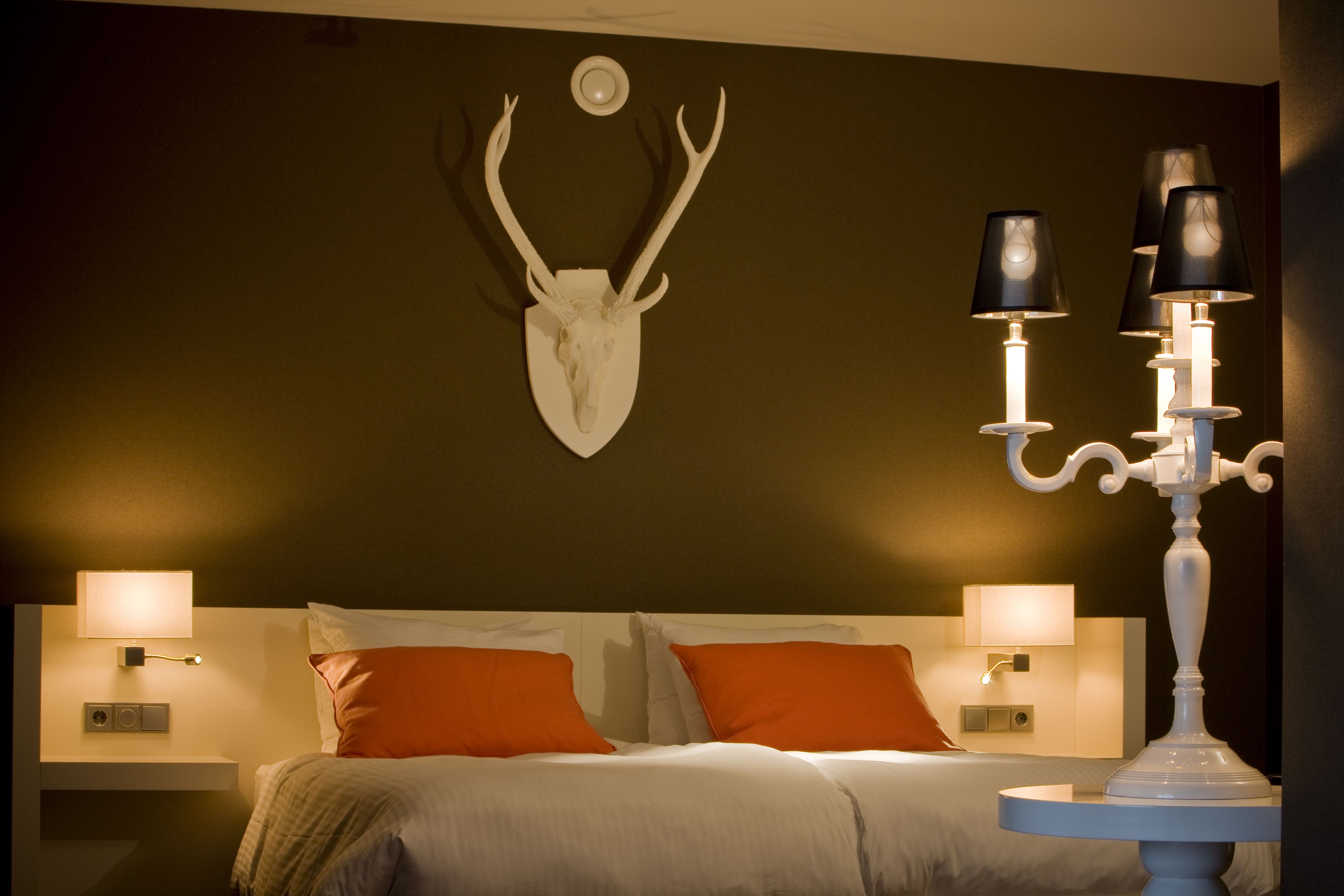 A hotel room with a bed, two nightstands, a wall-mounted deer skull, and a candelabra.
