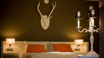 A hotel room with a bed, two nightstands, a wall-mounted deer skull, and a candelabra.