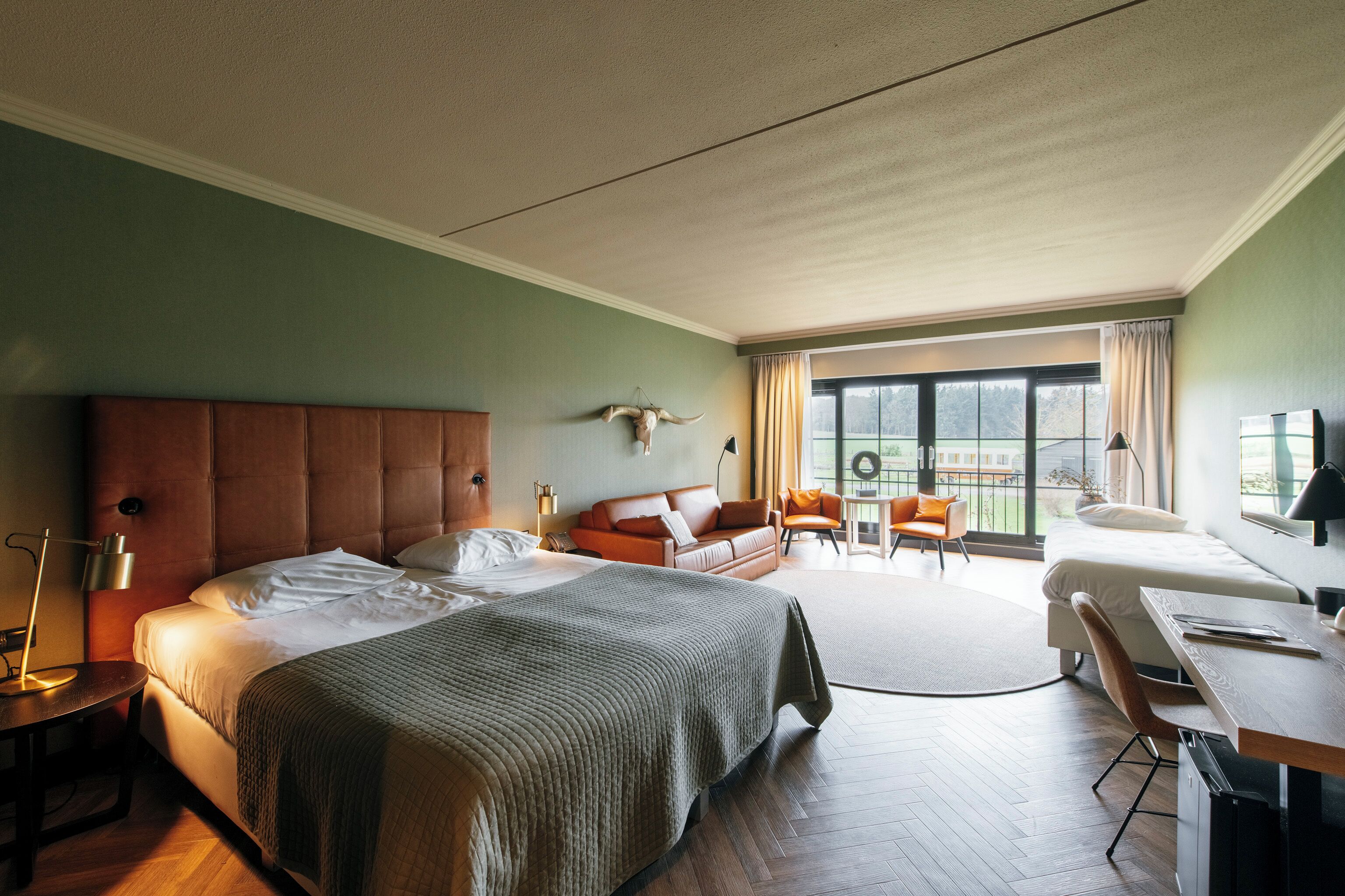 A modern hotel room with a large bed, a sofa, a desk, and a balcony with a view.