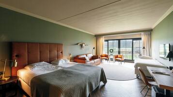 A modern hotel room with a large bed, a sofa, a desk, and a balcony with a view.