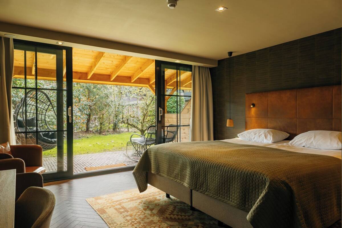 Un dormitorio con una cama grande, techo de madera y una puerta corrediza de vidrio que da a un patio con mobiliario exterior.