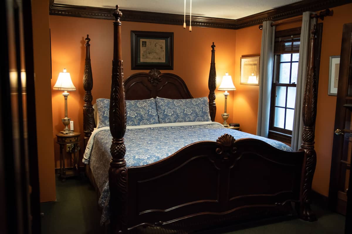 A four-poster bed with a floral bedspread, two bedside lamps, and a framed picture on the wall.