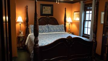 A four-poster bed with a floral bedspread, two bedside lamps, and a framed picture on the wall.