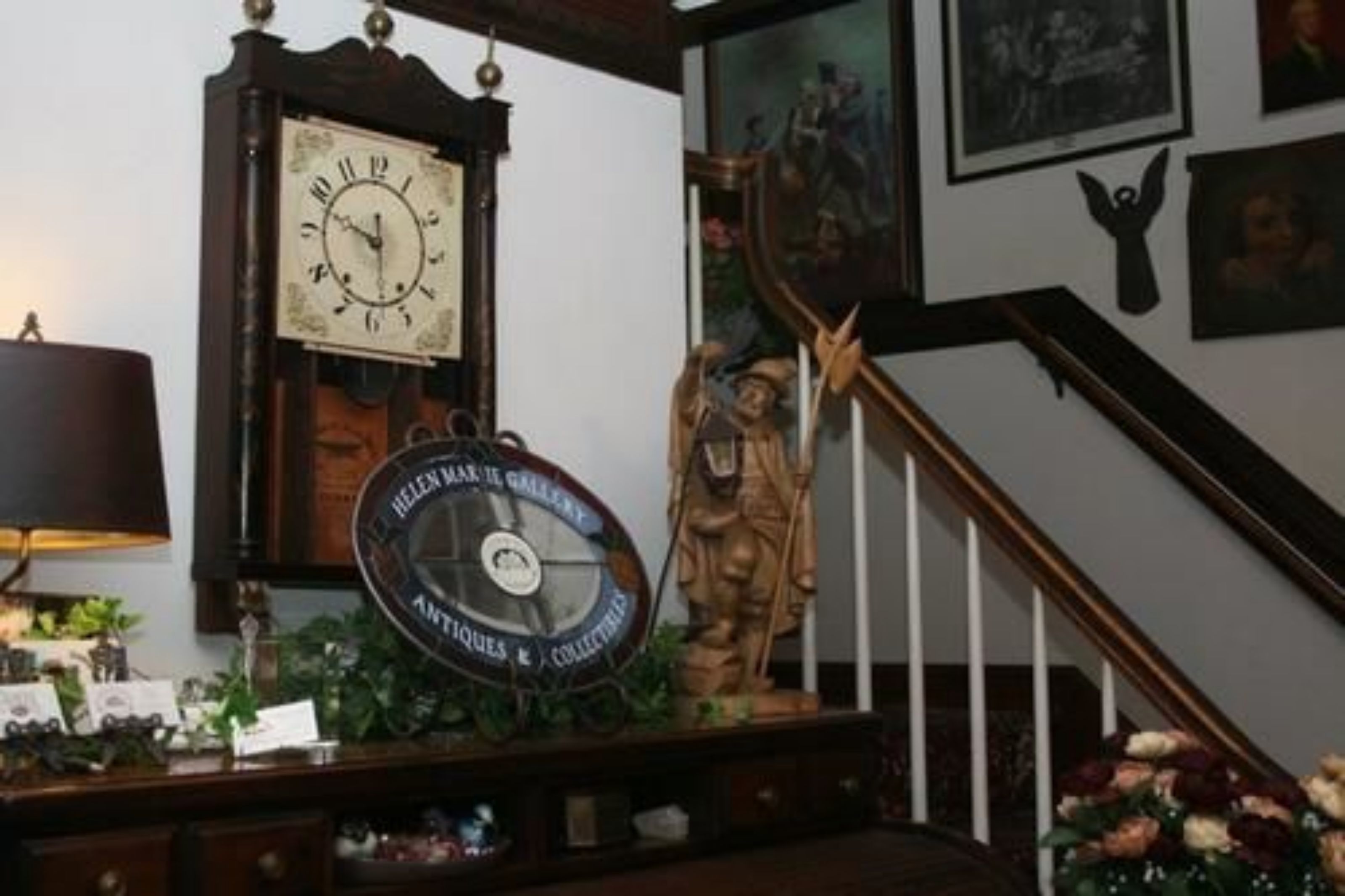 Une pièce avec un escalier en bois, une horloge et une statue.