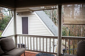A covered porch with two chairs, a small table, and a view of a house with a dark door and a sloped roof. - Williamsburg Sampler B & B (Williamsburg)