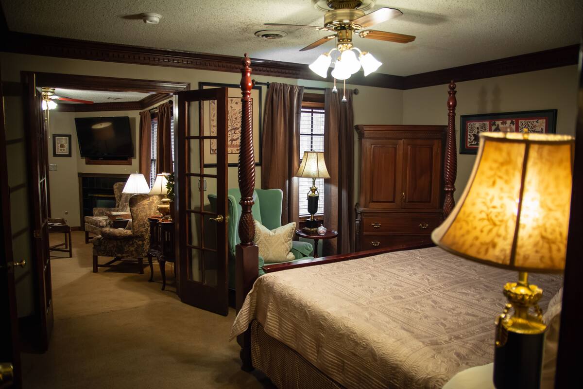 A bedroom with a bed, a ceiling fan, a lamp, and a chair.