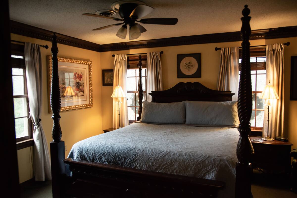 A four-poster bed with a wooden headboard, a ceiling fan, and two bedside lamps.