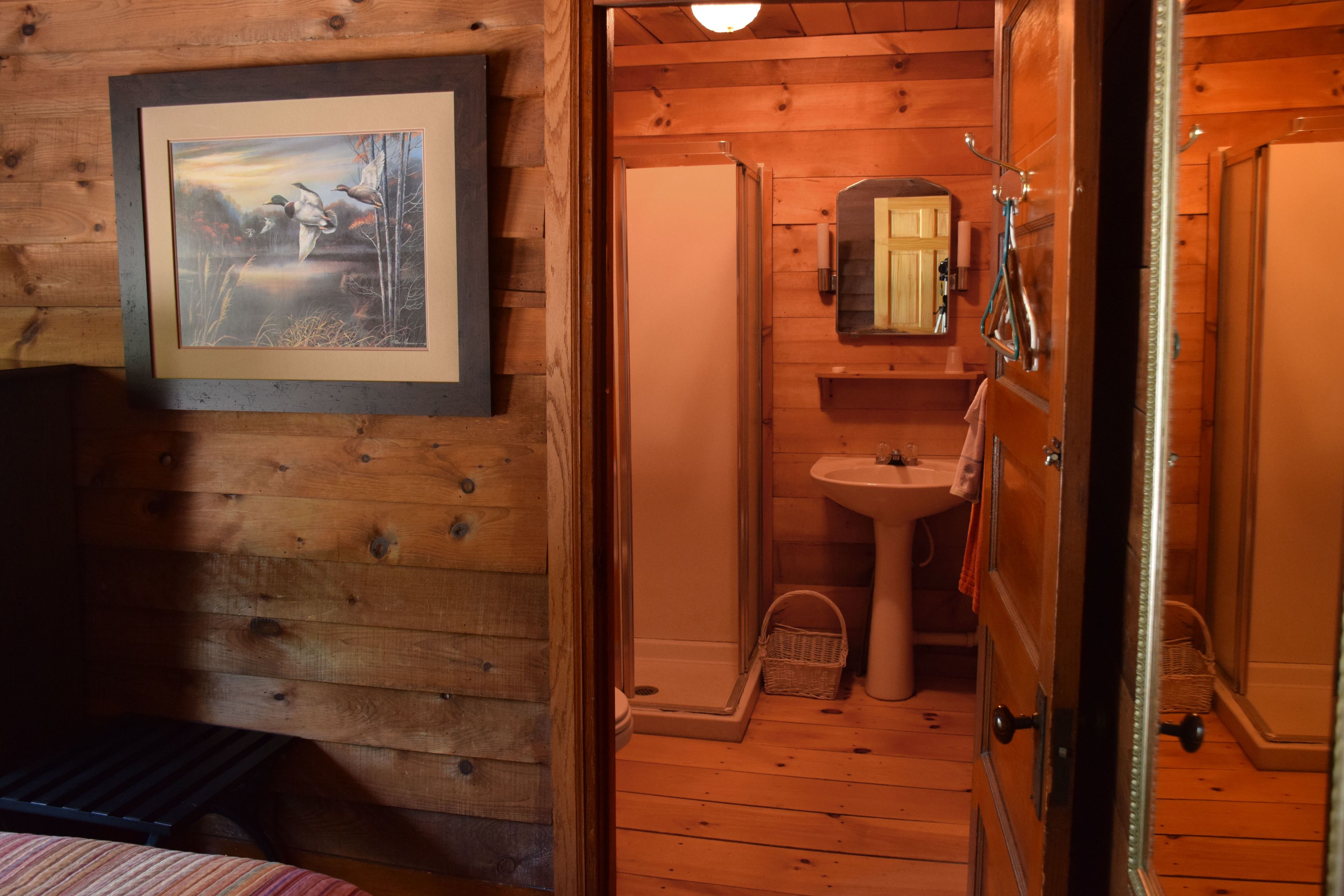 A wooden cabin bathroom with a framed picture on the wall, a sink, and a door leading to another room.