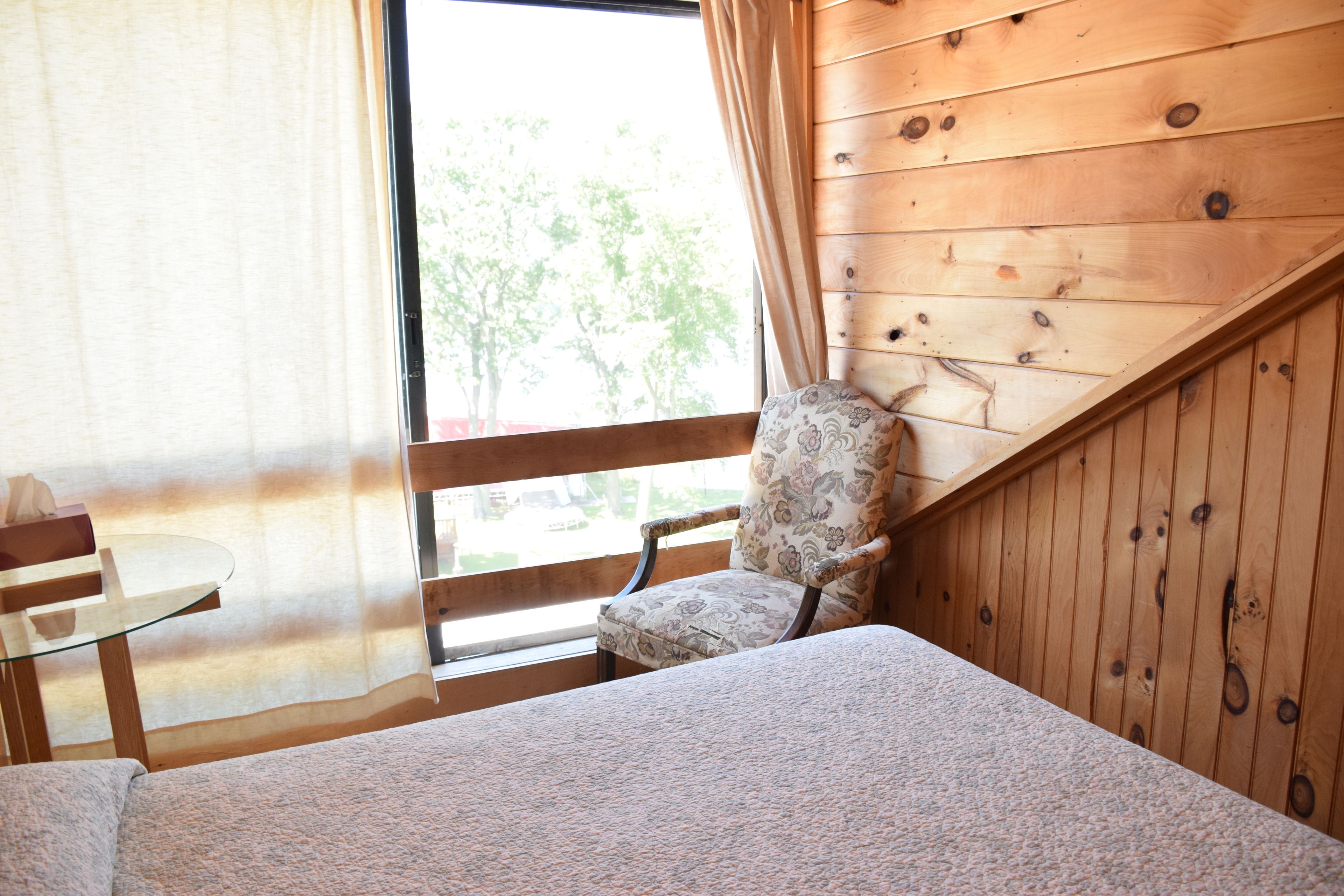 Una habitación con una cama, una silla, una mesita y una ventana con cortinas.