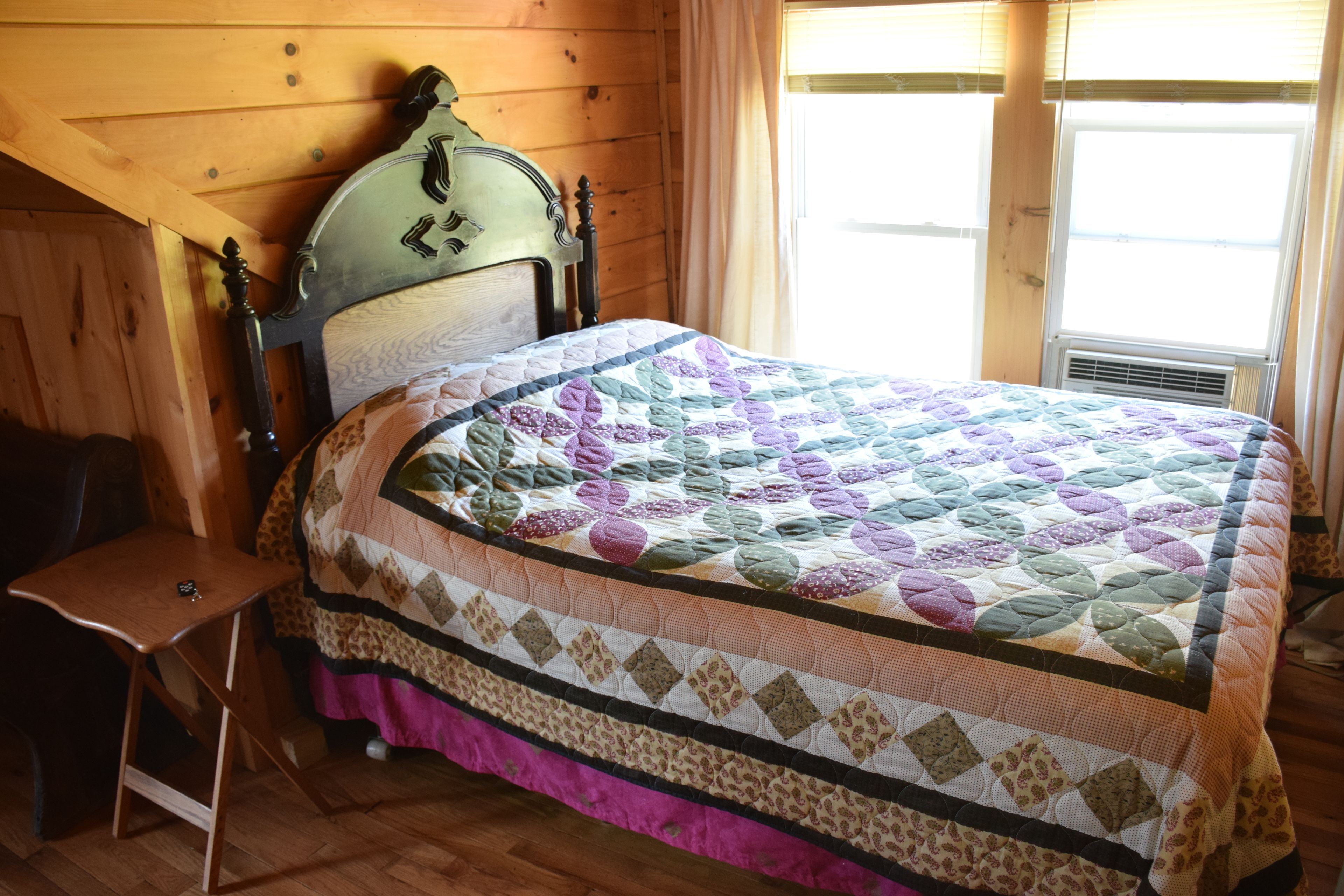A wooden cabin room with a bed, a chair, and a window.