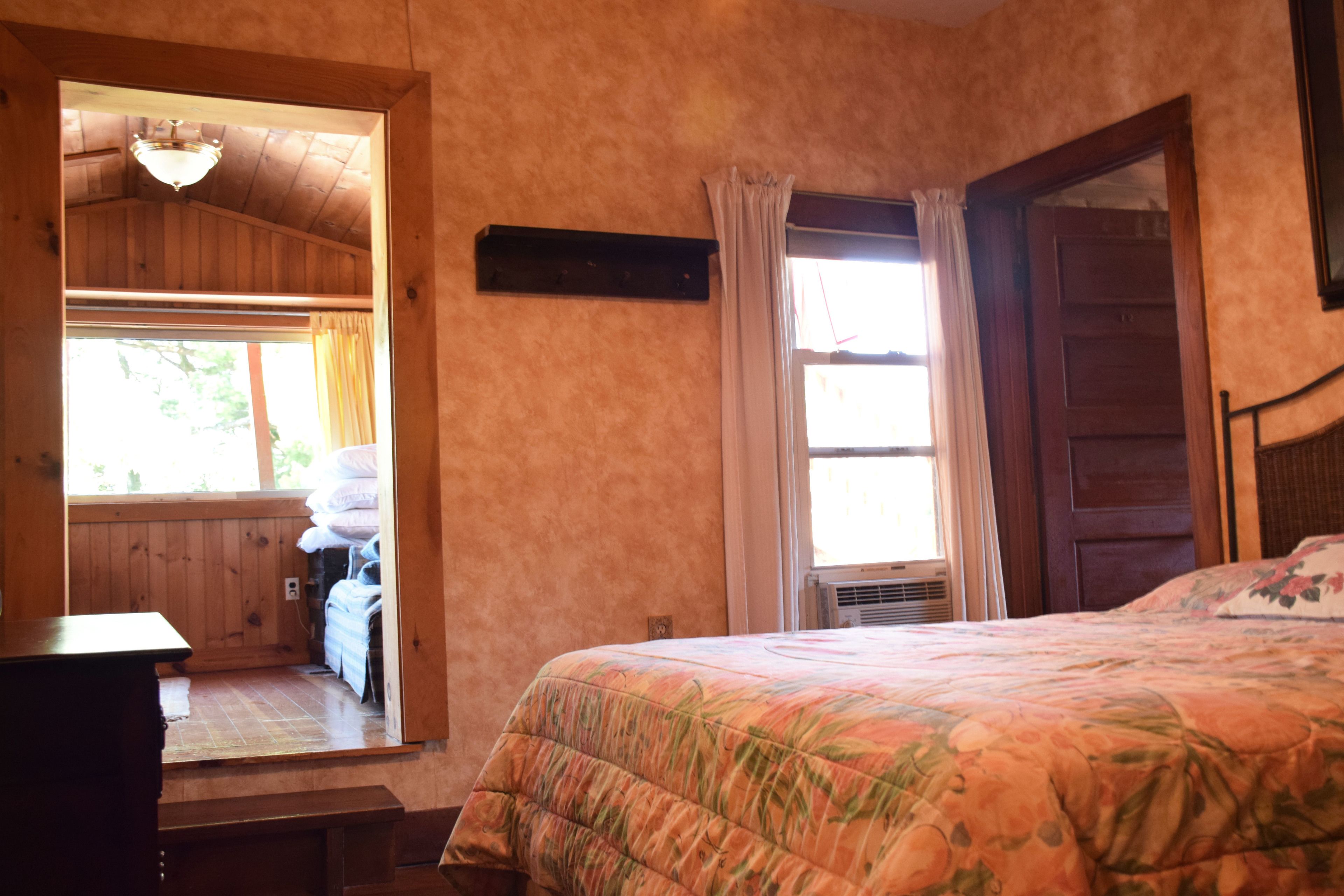 Quarto com cama, paredes de madeira, janela com cortinas e porta.
