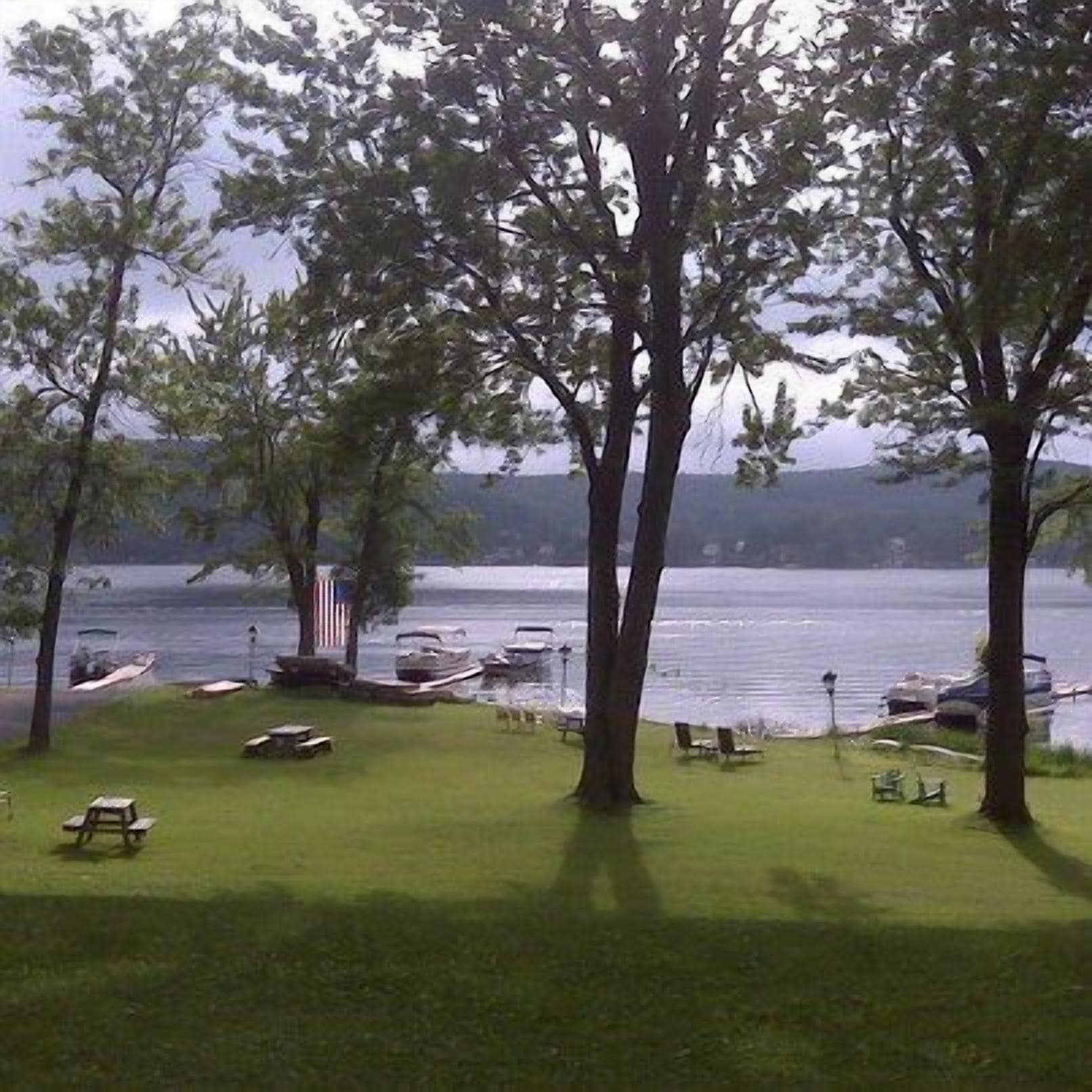 A lakeside view with trees, boats, and picnic tables.