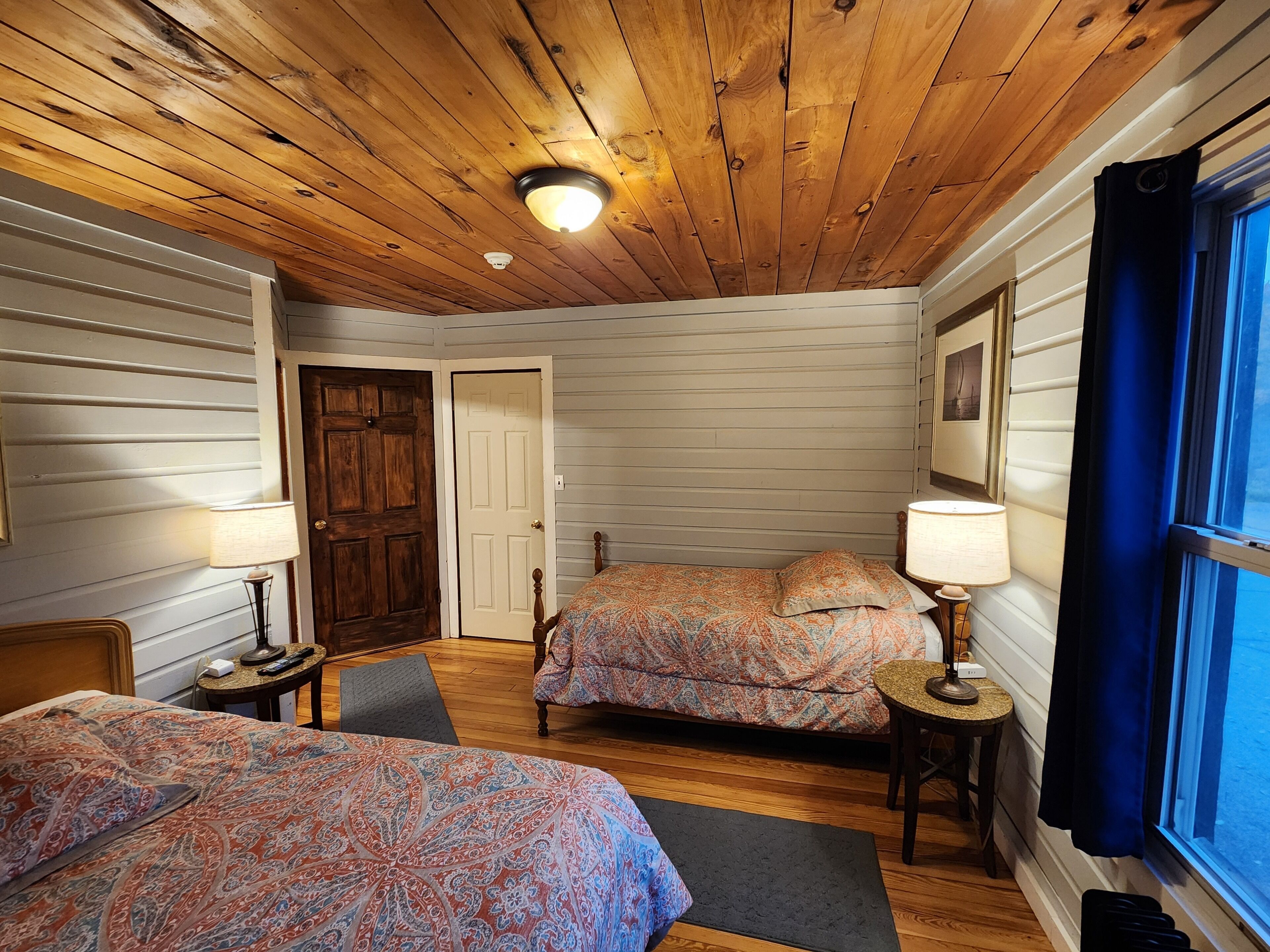A cozy room with two beds, wooden ceiling, and a window with curtains.