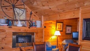 A cozy cabin interior with a fireplace, wooden walls, a television, and a lamp.