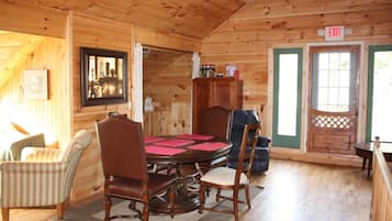 A wooden cabin interior with a dining table, chairs, a framed picture, and an exit sign.