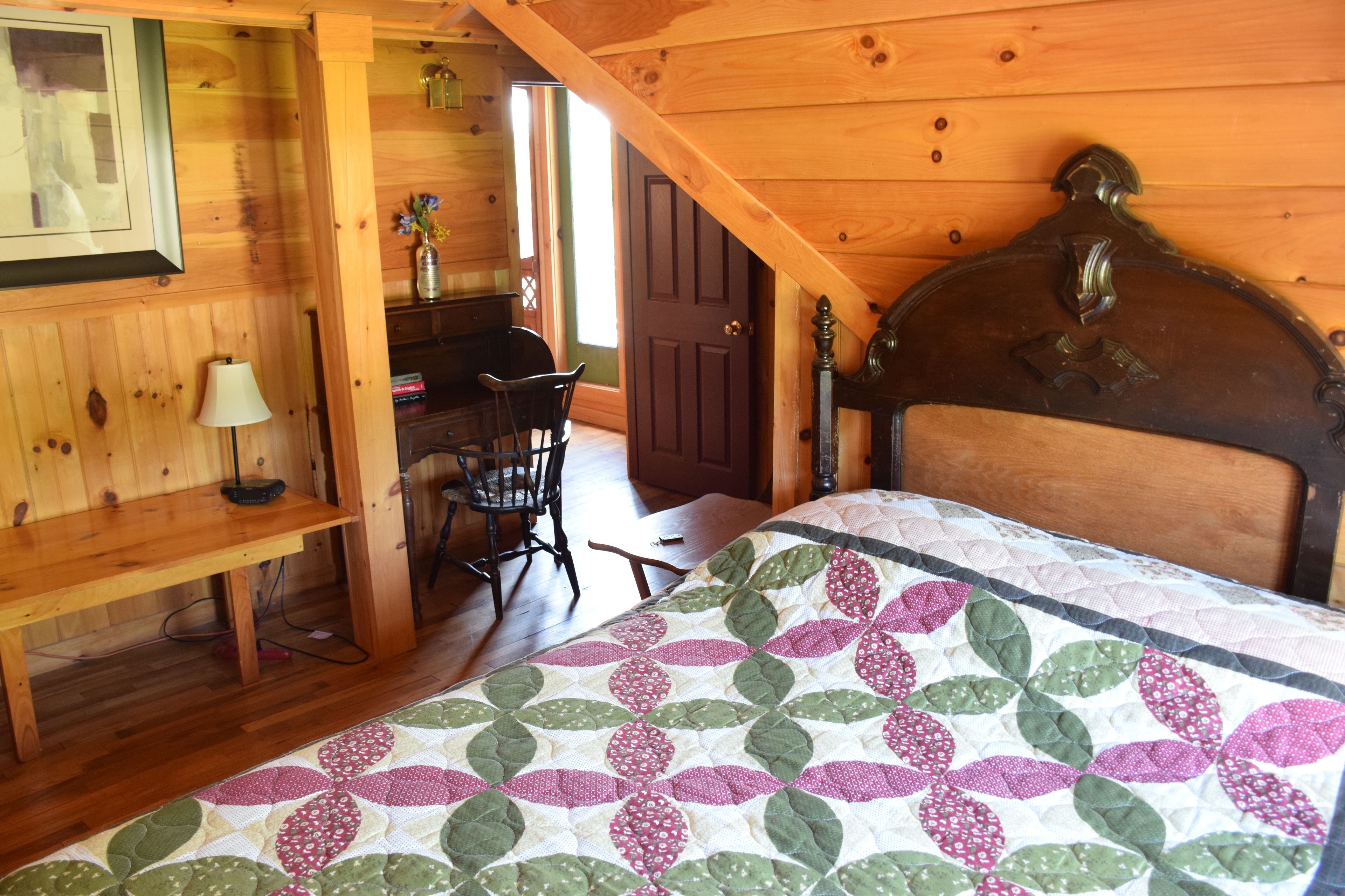 Una habitación acogedora con techo de madera, una cama con colcha estampada, un escritorio con silla y una lámpara.