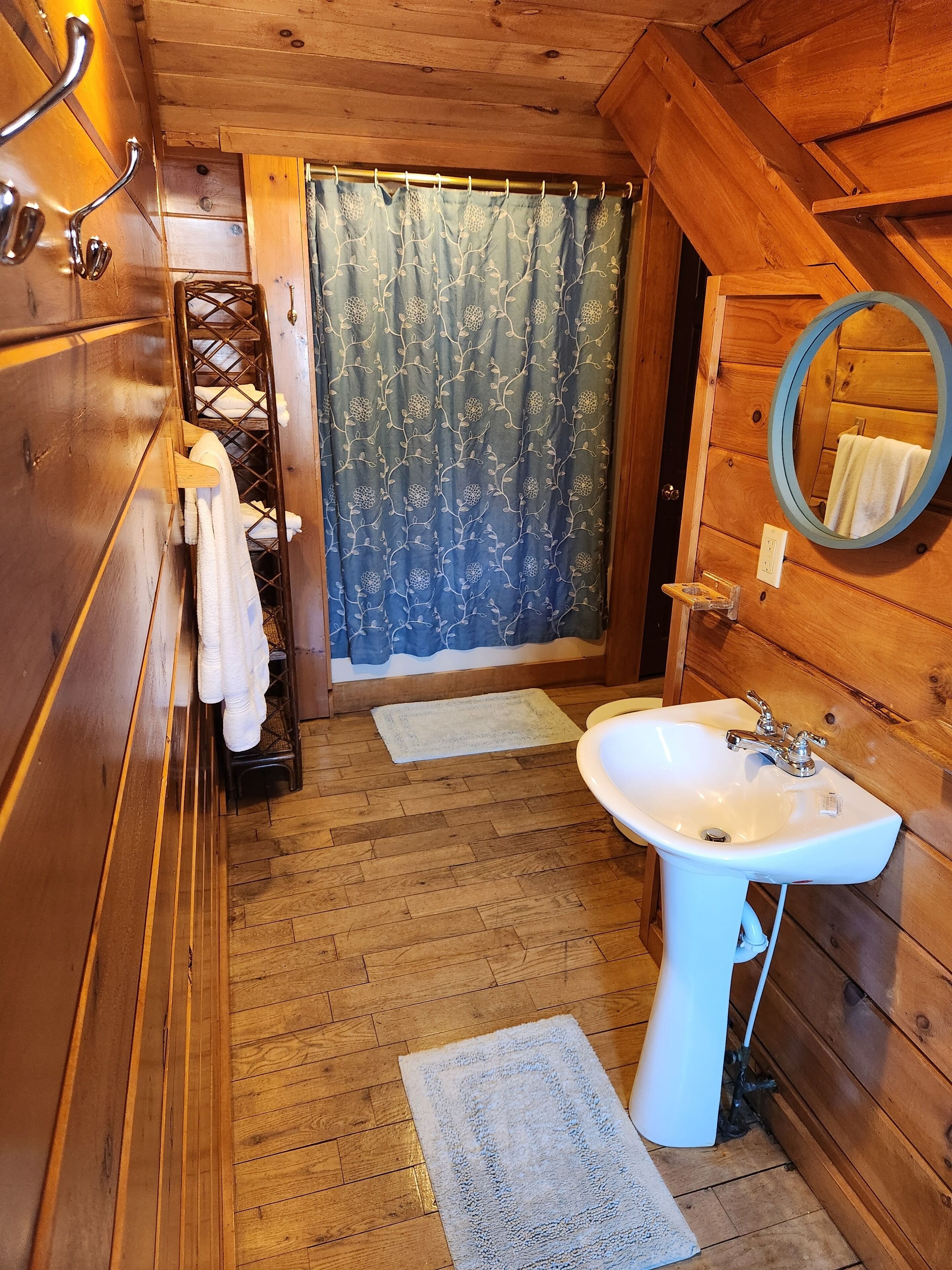 A wooden cabin bathroom with a wooden sink, a mirror, a towel rack, and a shower curtain.