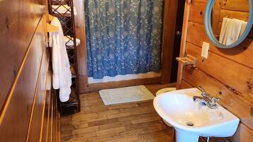 A wooden cabin bathroom with a wooden sink, a mirror, a towel rack, and a shower curtain.