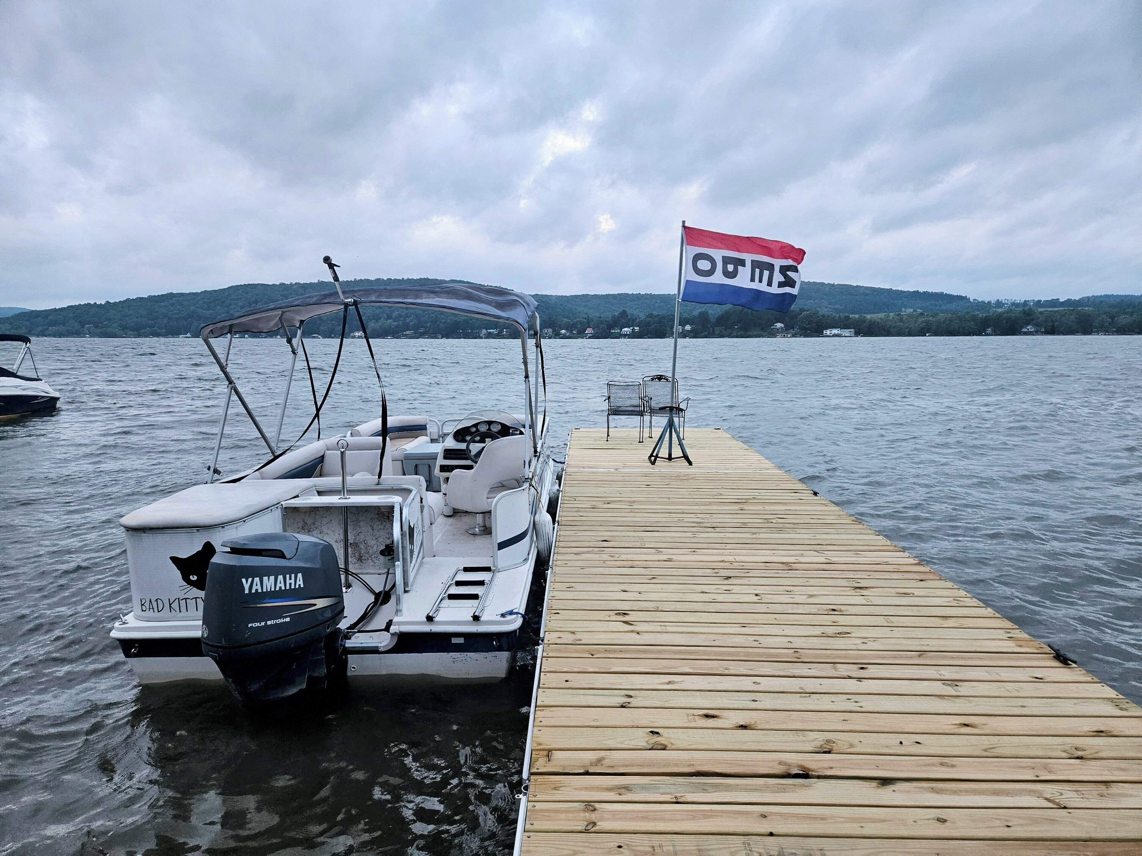 Un bote amarrado en un muelle de madera con un motor fueraborda Yamaha, una bandera y una silla.