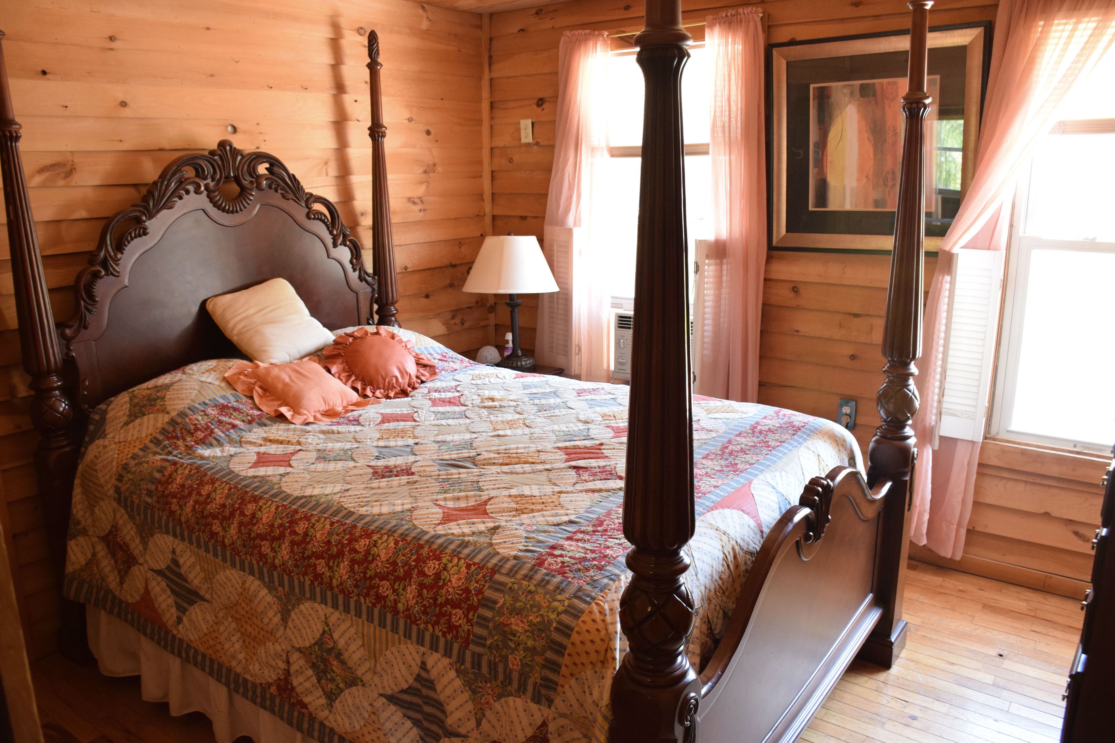 A four-poster bed with a floral quilt, a nightstand with a lamp, and a framed picture on the wall.