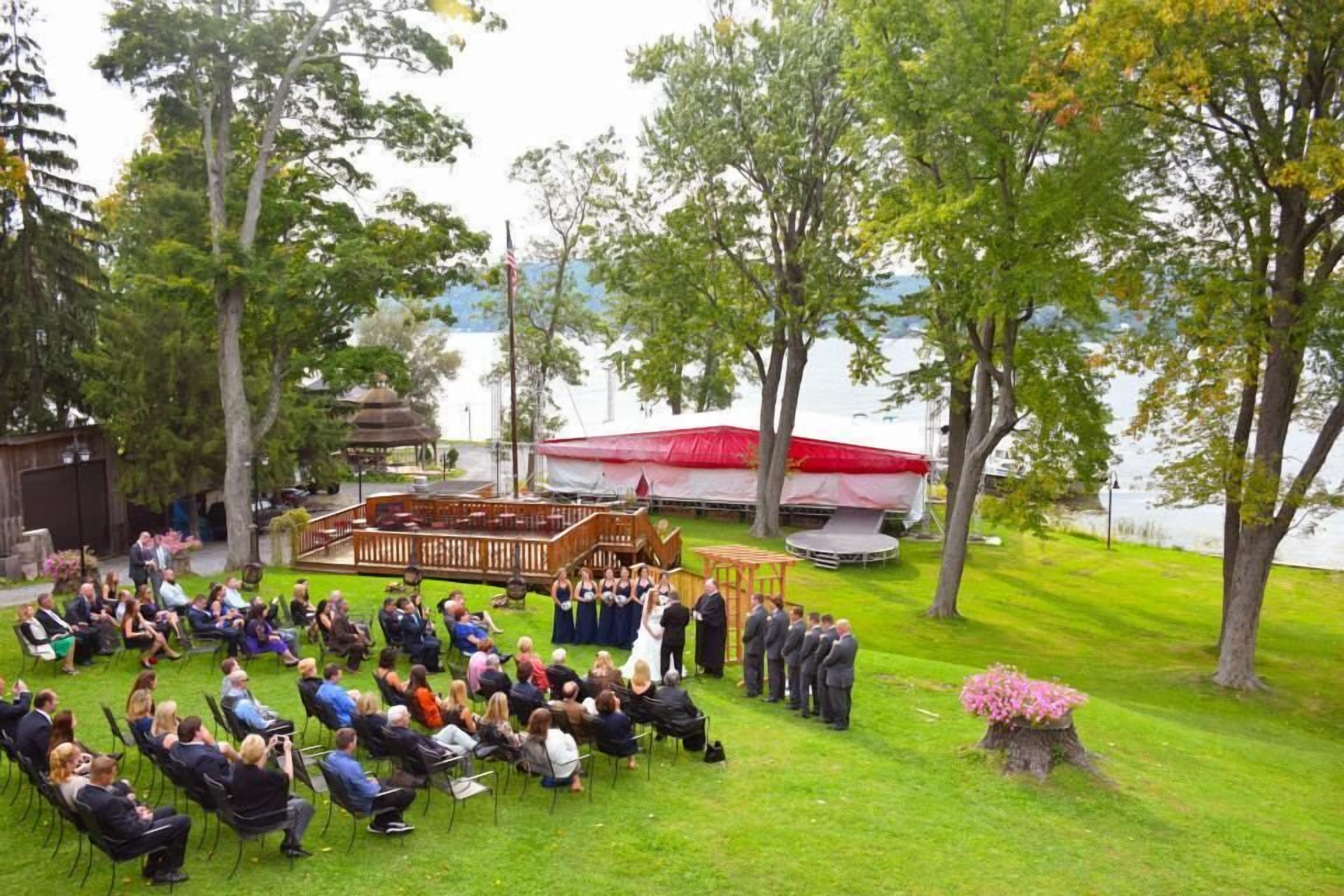 An outdoor wedding ceremony with guests seated on chairs arranged in rows facing a wooden stage.
