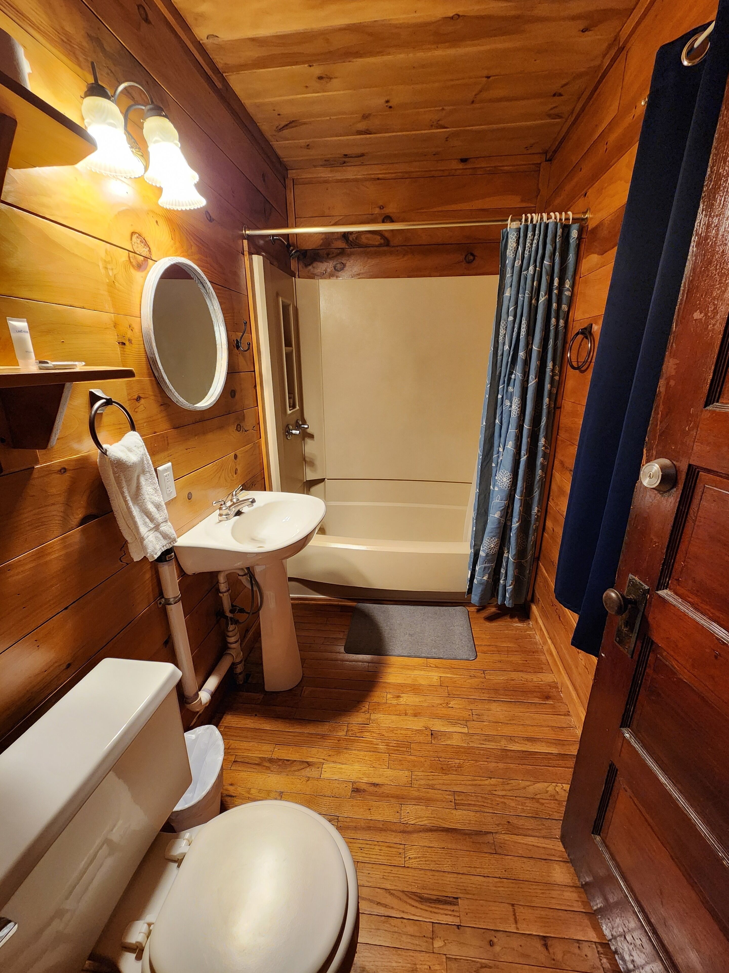 Une salle de bain rustique, aménagée dans une cabane en bois, avec des toilettes, un lavabo et une douche.