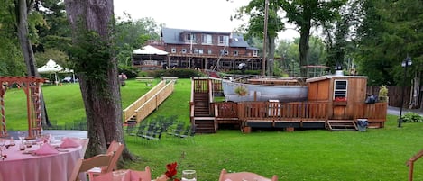 A dining area with pink tablecloths and glassware, set against a backdrop of a wooden deck and a building with a covered patio.