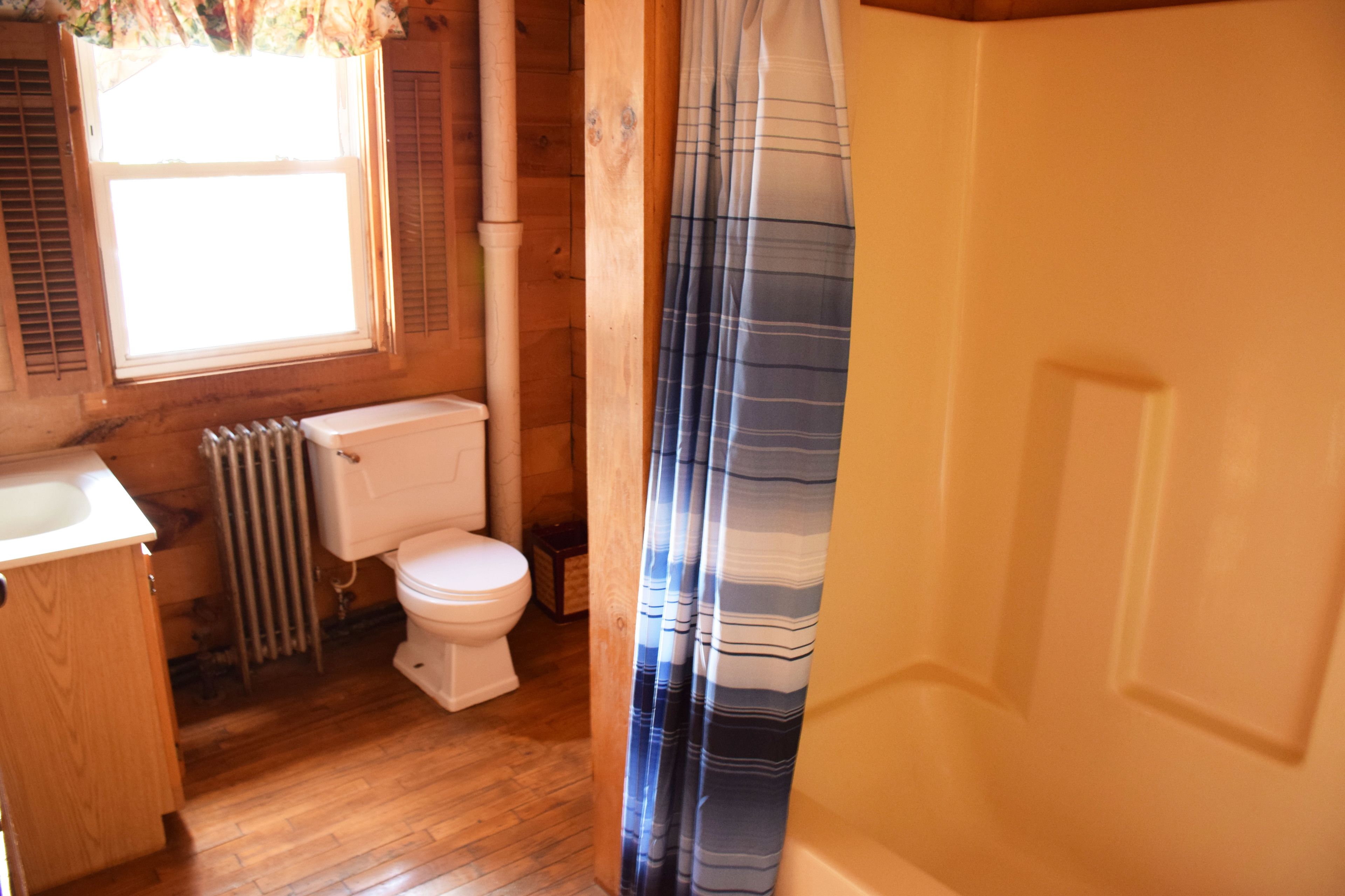 Un baño con paredes de madera, un inodoro, un radiador y armarios de madera.