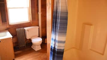 Un baño con paredes de madera, un inodoro, un radiador y armarios de madera.