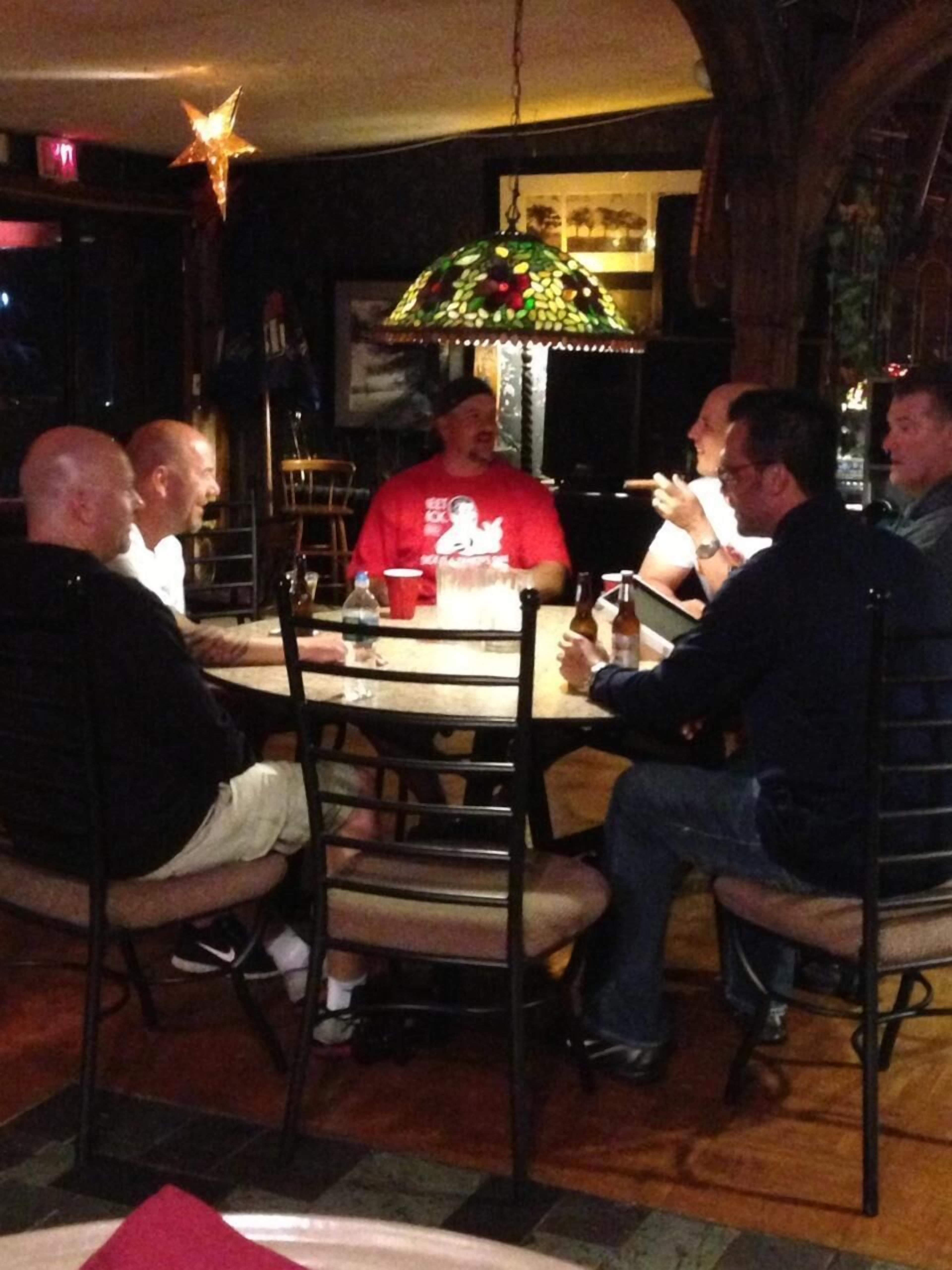 A group of people seated around a round table in a dimly lit room with a decorative hanging lamp.