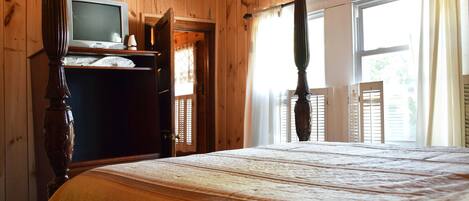 A wooden-paneled bedroom with a bed, a television on a dresser, and a window with shutters.