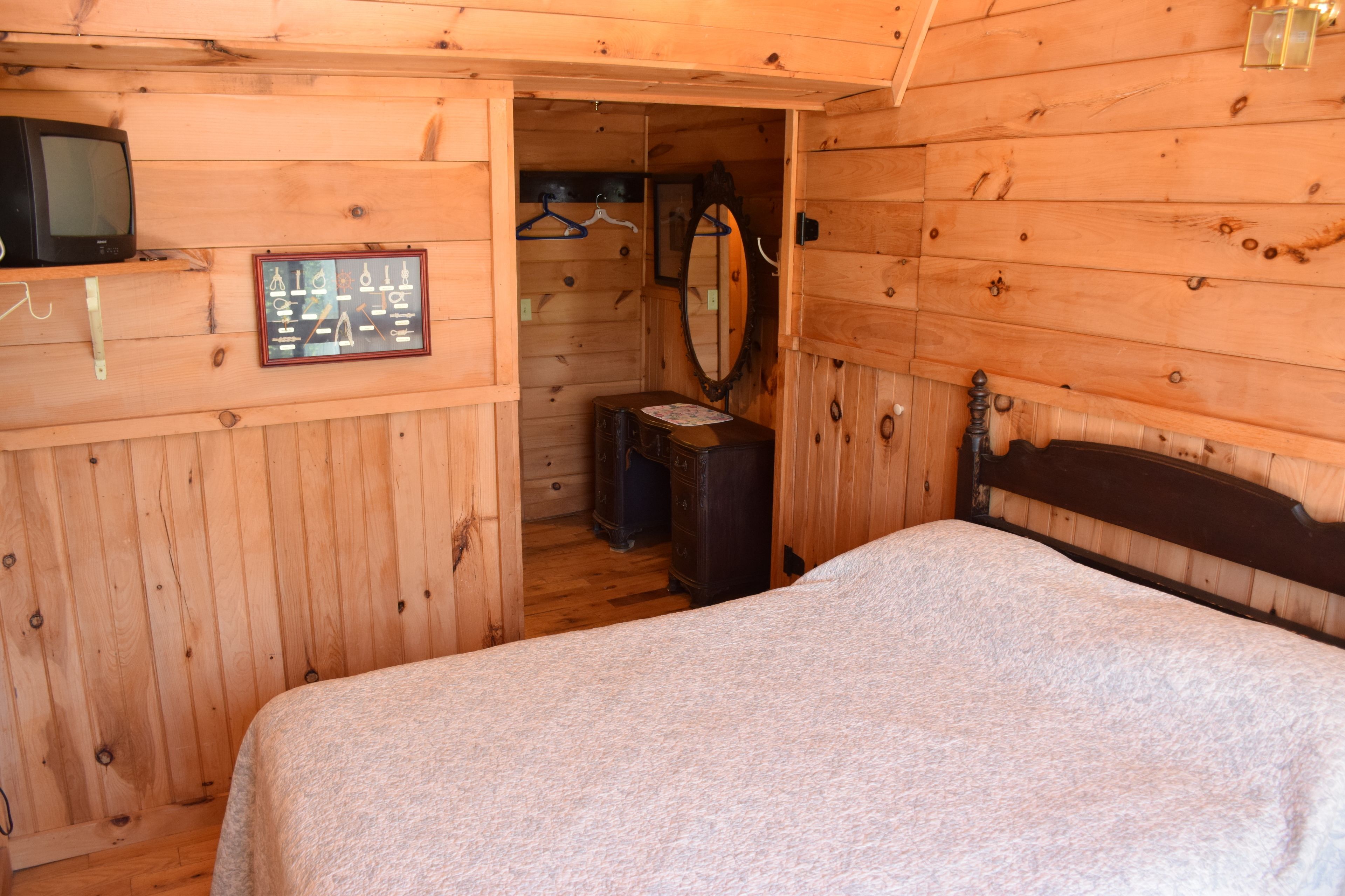 Une chambre dans une cabane en bois, avec un lit, une commode, un miroir et une petite télévision posée sur une étagère.