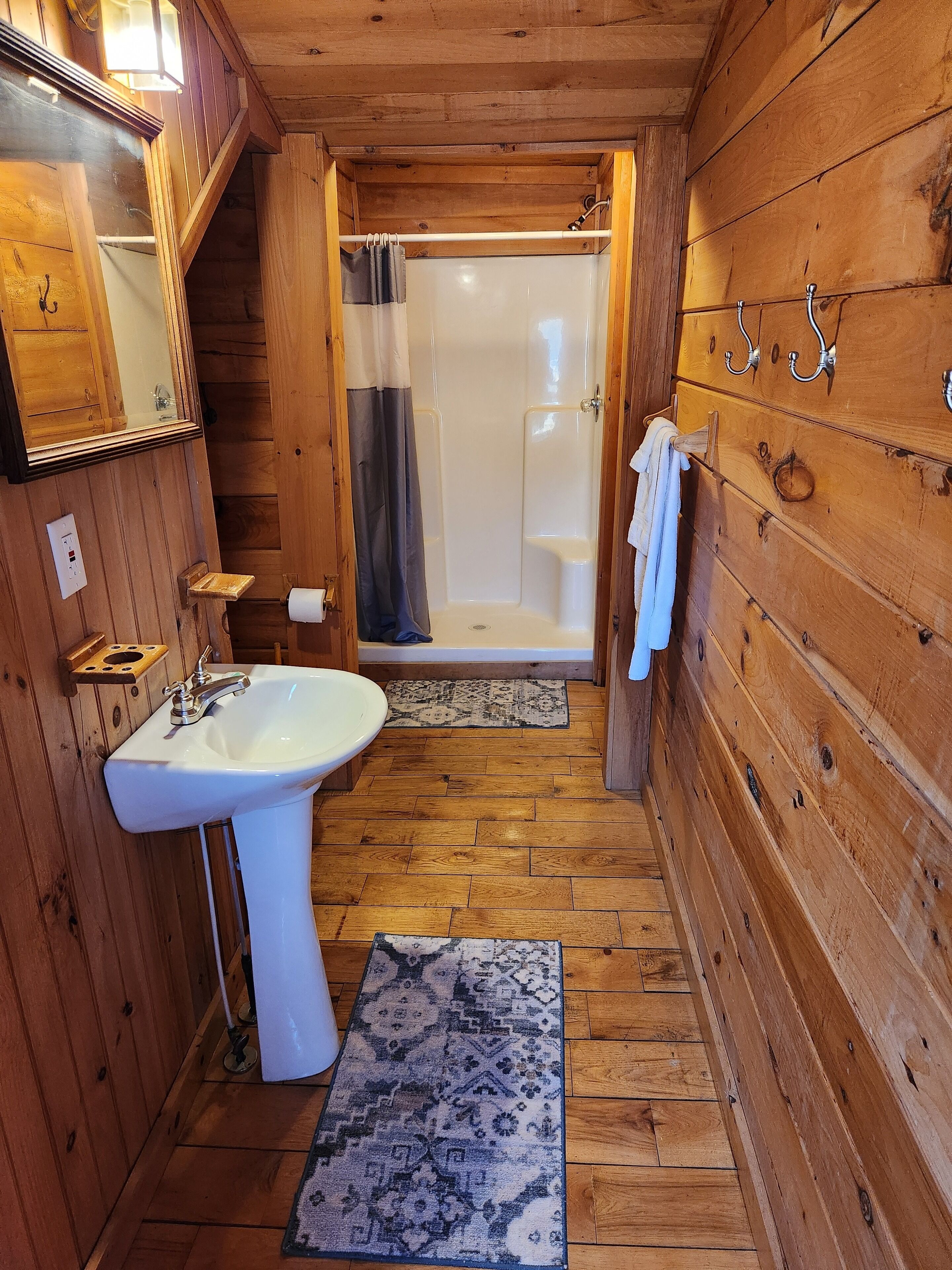 A wooden cabin bathroom with a white sink, a shower, and a wooden floor.