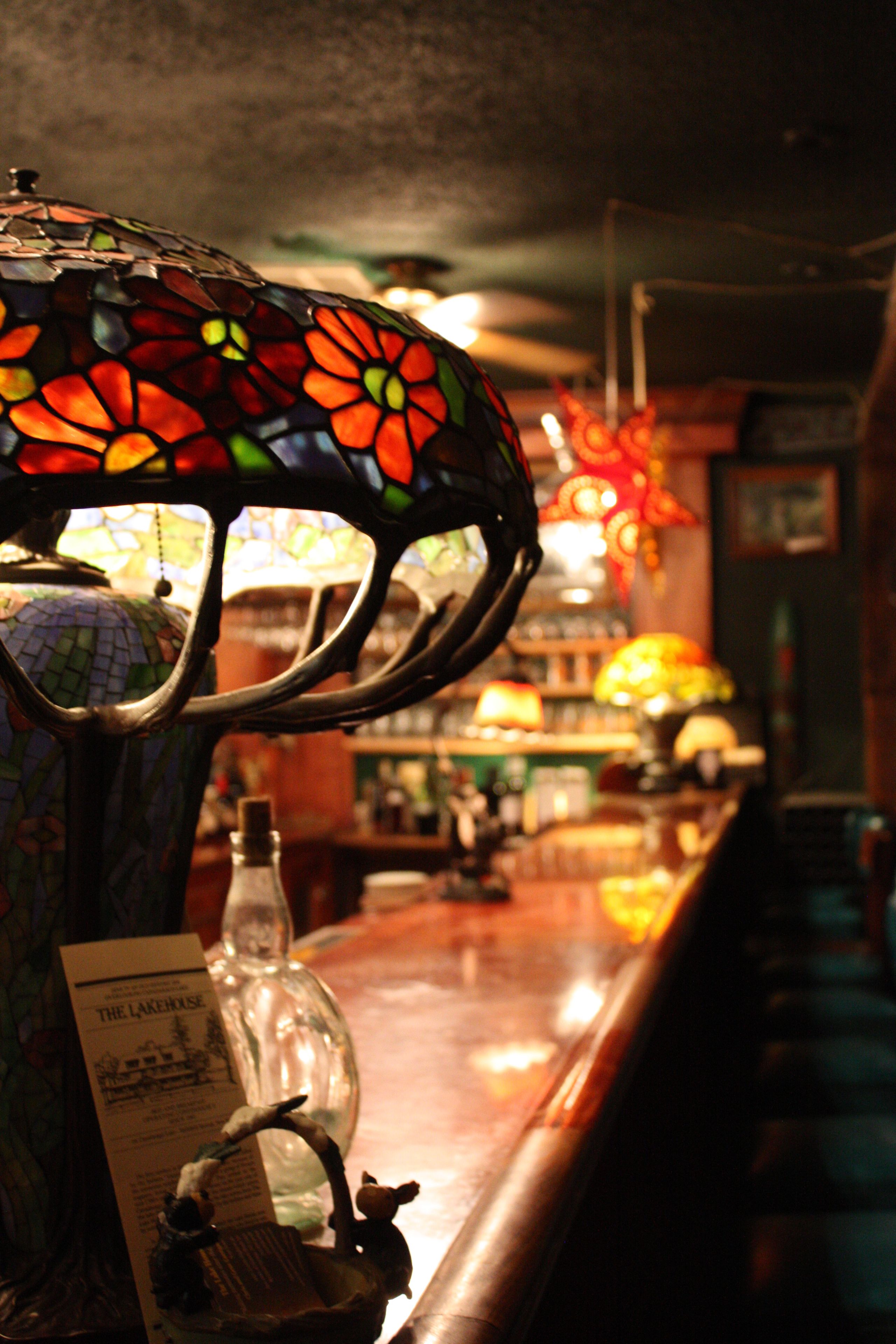 Eine Bar mit einer Lampenschirm aus Buntglas, einer Flasche und einem Menüschild.