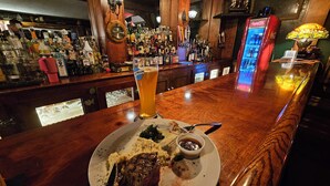 A bar with a wooden counter, a glass of beer, and a plate with food remnants.