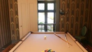 A pool table with balls and cues, a wooden cabinet, and a window with a view of a balcony. - Rock Hall Luxe Lodging (Winsted)
