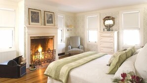 A bedroom with a fireplace, a bed with a green blanket, a chair, and a dresser. - Rock Hall Luxe Lodging (Winsted)