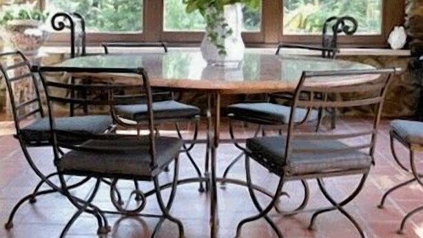 A stone archway leading to a dining area with a round table and chairs, a vase with flowers, and a view of greenery through large windows. - Rock Hall Luxe Lodging (Winsted)