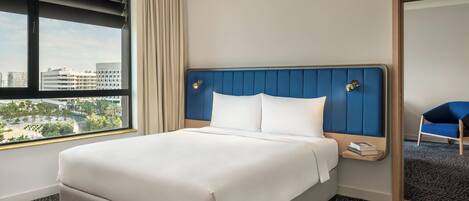 A hotel room with a large bed, a view of the city, and a blue chair.