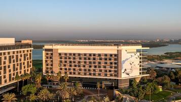 A modern hotel with a central courtyard, surrounded by palm trees and a view of a body of water.